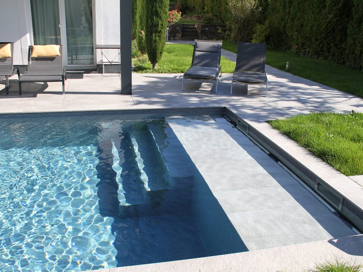 Piscine familiale avec des plages grises, couverte par un volet immergé.