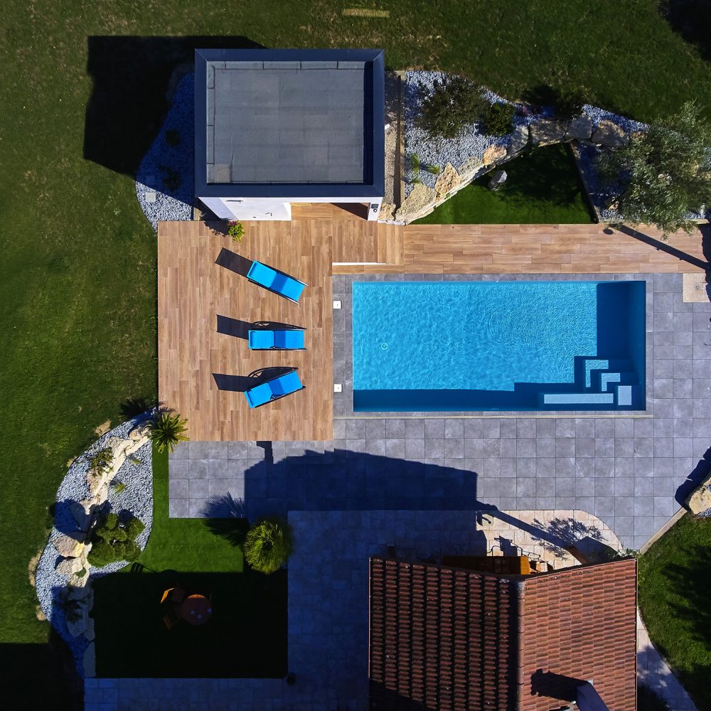 Vue de jour sur une piscine classique avec abri extra-plat et terrasse en grès cérame