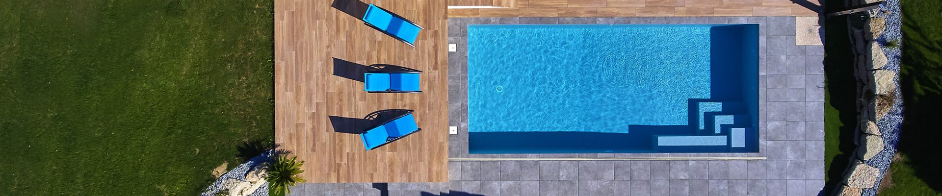 Vue de jour sur une piscine classique avec abri extra-plat et terrasse en grès cérame