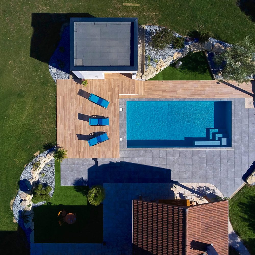 Vue de jour sur une piscine classique avec abri extra-plat et terrasse en grès cérame