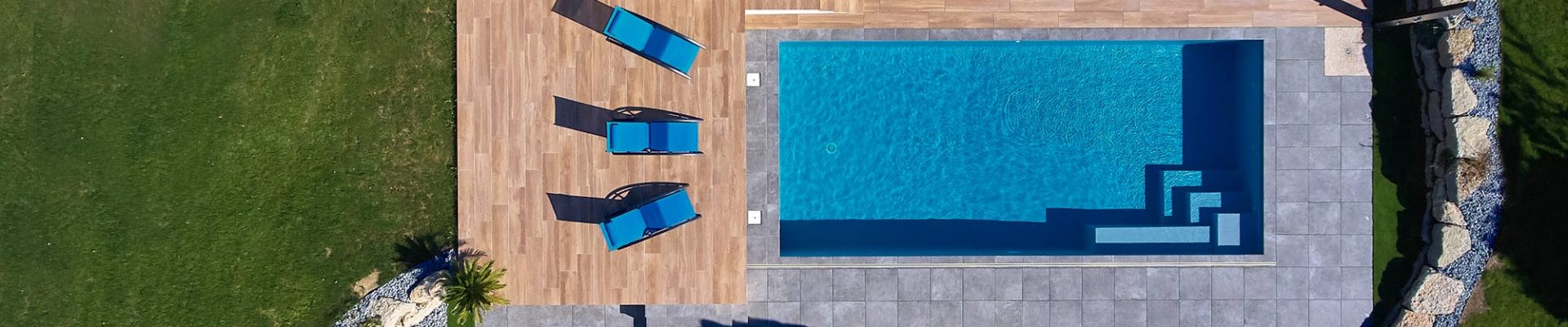 Vue de jour sur une piscine classique avec abri extra-plat et terrasse en grès cérame